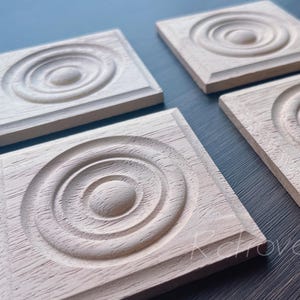 Puede incluir: Cuatro posavasos cuadrados de madera con un diseño de círculos concéntricos tallados. Los posavasos son de madera de color claro y tienen un borde elevado. El diseño presenta un círculo central elevado rodeado de anillos concéntricos.