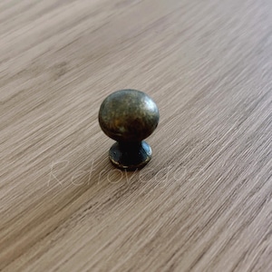 May include: A round, antique brass cabinet knob with a smooth, slightly domed surface.