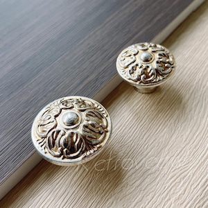 May include: Two ornate silver and gold cabinet knobs with a floral design.