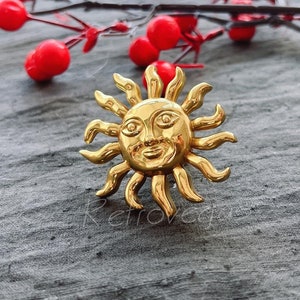 Puede incluir: Un sol de color dorado con una cara y rayos, sobre una superficie gris texturizada.