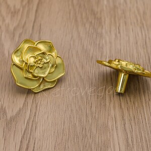 May include: Two gold-toned cabinet knobs with a floral design. The knobs are shaped like roses with intricate details.