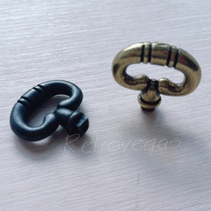 May include: Two decorative key-shaped drawer pulls. One is black metal and the other is gold metal.