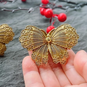 May include: Two gold butterfly brooches with intricate details. The brooches are made of metal and have a shiny finish.