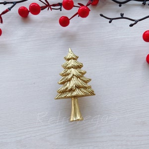 May include: A gold-colored metal Christmas tree ornament with a detailed design. The ornament is on a white background.