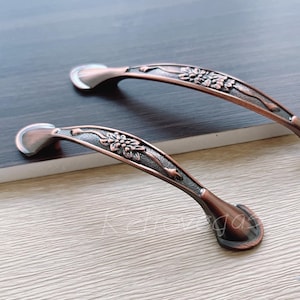 Può includere: Due maniglie per ante di armadio in rame antico con un design floreale.