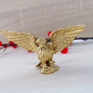 May include: A gold eagle figurine with its wings spread wide. The eagle is perched on a small base and has a detailed design.