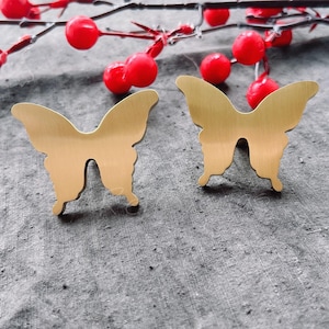 May include: Two gold butterfly-shaped drawer pulls. The pulls are on a grey fabric background.