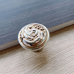 May include: A silver and gold cabinet knob with a swirling design.