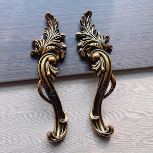 May include: Two ornate gold-toned metal drawer pulls with a decorative floral design.