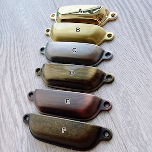 Peut inclure: Six poignées de tiroir différentes dans différentes finitions, notamment le laiton poli, le laiton brossé, le nickel, le laiton antique, le cuivre et le laiton vieilli. Les poignées sont toutes de la même forme, un rectangle incurvé légèrement arrondi avec un petit trou à chaque extrémité pour le montage.