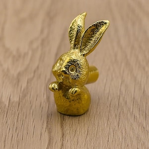 May include: A gold-colored rabbit figurine with a detailed design. The rabbit is standing on a wooden surface.