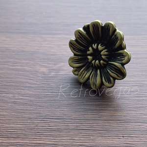 May include: A gold-toned metal flower-shaped cabinet knob with a dark brown centre.