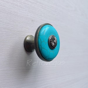 May include: A turquoise blue cabinet knob with a silver metal base and a decorative silver flower design in the center.
