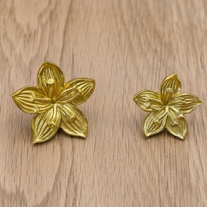 May include: Two gold-coloured metal flower-shaped drawer pulls. The larger pull is on the left and the smaller pull is on the right.