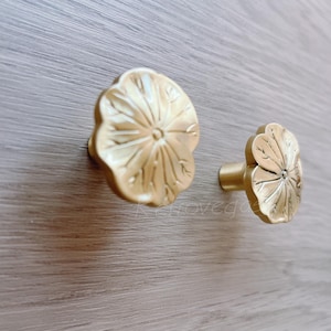 May include: Two gold-toned flower-shaped cabinet knobs with a detailed floral design.