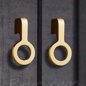 May include: Two gold cabinet door pulls with a circular design. The pulls are mounted on a black surface.