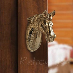 May include: A gold-toned horse head door handle. The handle is mounted on a wooden door.