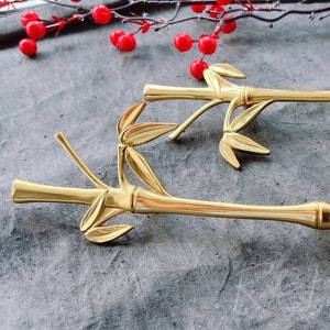 May include: Two gold-toned cabinet pulls shaped like bamboo with detailed leaf accents.