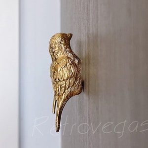 May include: A gold-coloured bird-shaped door handle mounted on a light brown wooden door.