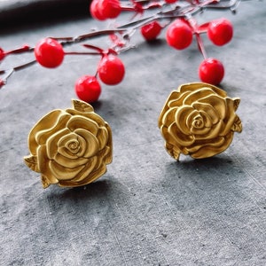 May include: A pair of gold-tone rose-shaped earrings. The earrings are made of metal and have a detailed design.