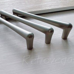 May include: Three silver cabinet pulls with a brushed finish. The pulls are in a row, with the largest pull on the left and the smallest pull on the right.