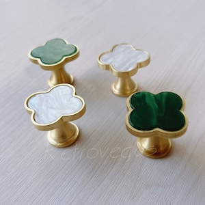 May include: Four gold-toned cabinet knobs in a clover shape. Each knob has a different coloured insert: green, white, green, and white.