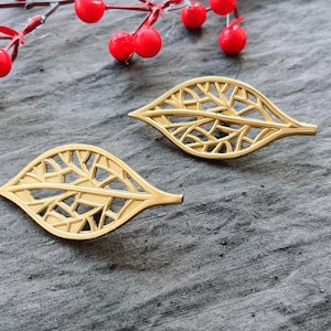 May include: A pair of gold leaf-shaped earrings with a delicate, intricate design. The earrings are made of metal and have a shiny finish.