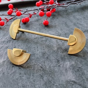 Puede incluir: Herrajes de armario de color dorado con un diseño en forma de abanico. Los herrajes se muestran sobre un fondo gris oscuro.