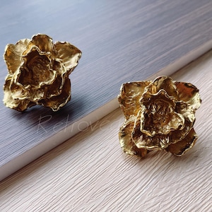 May include: Two gold-toned metal flower-shaped drawer pulls. The pulls have a textured, organic design.