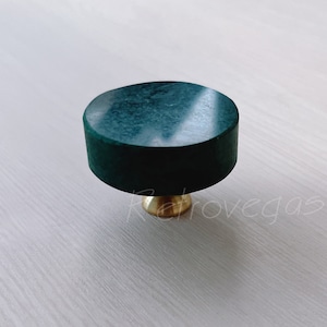 May include: A dark green marble cabinet knob with a brass base. The knob is round and has a polished finish. The brass base is a warm gold color. The knob is a decorative hardware element.