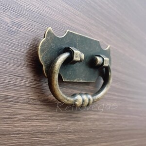 Könnte beinhalten: Ein antiker, verzierter, schwarzer Metall-Schubladenzug mit einem Ringgriff. Der Zug hat eine patinierte Oberfläche und ist dazu bestimmt, Möbeln einen rustikalen Charme zu verleihen.