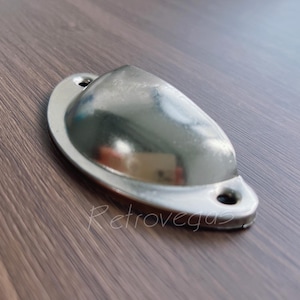 May include: A silver metal drawer pull with a rounded, slightly curved shape. The pull has two small holes for mounting.