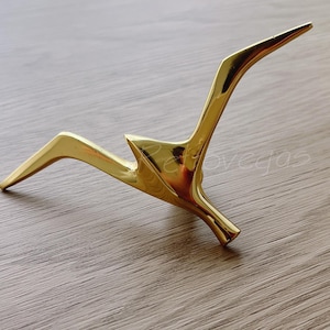May include: A gold-colored metal sculpture of a bird in flight. The sculpture is abstract and has a modern design.