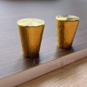 May include: Two gold-toned hammered metal cabinet knobs. The knobs are cone-shaped and have a textured surface.