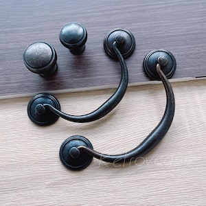May include: Four black metal cabinet door pulls. Two are round with a single screw hole. Two are D-shaped with a curved handle and two screw holes.
