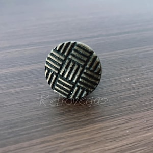 May include: A round, antique brass-colored cabinet knob with a woven pattern. The knob is centered in the image and sits on a dark wood surface. The word "Retrovegas" is faintly visible.