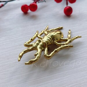 May include: A gold-coloured beetle brooch with intricate details. The brooch is made of metal and has a shiny finish.