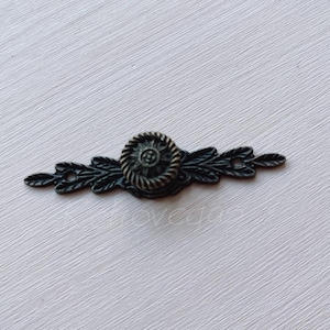 Puede incluir: Un tirador de cajón de metal negro con un diseño floral decorativo y un pomo redondo en el centro.