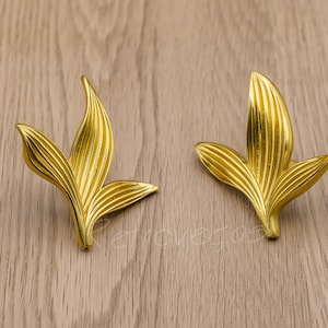 May include: Two gold leaf-shaped cabinet pulls with a textured surface.