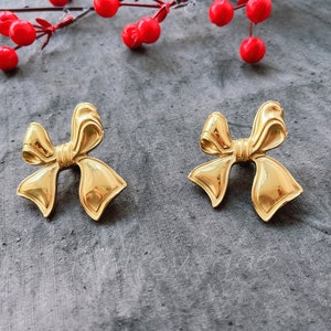 May include: A pair of gold-tone bow-shaped earrings. The earrings are made of metal and have a shiny finish.