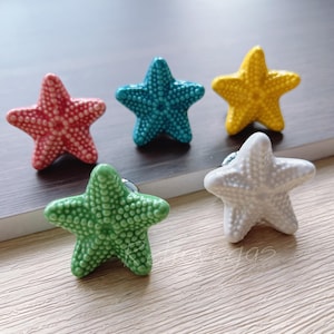 May include: Five ceramic starfish drawer pulls in various colors, including red, blue, yellow, green, and white. The starfish are all the same size and have a textured surface.