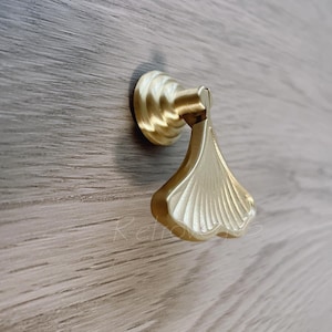 May include: Gold-toned metal drawer pull with a ginkgo leaf design. The pull has a rounded base and a flat, leaf-shaped handle.