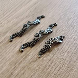 May include: Three ornate metal drawer pulls with a decorative scroll design. The pulls are a dark bronze color.