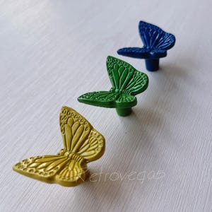 May include: Three butterfly-shaped cabinet knobs in yellow, green and blue. The knobs are made of metal and have a detailed butterfly design.