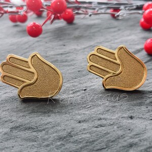 May include: A pair of gold-colored earrings in the shape of a hamsa hand, a symbol of protection and good luck.