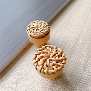 Pode incluir: Dois botões redondos de vime natural tecido com base de madeira. Os botões são de cor castanho claro e têm um padrão tecido.