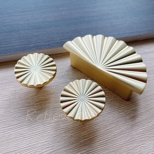 May include: Three gold-toned cabinet knobs with a fan-shaped design. The knobs are made of metal and have a smooth, polished finish.