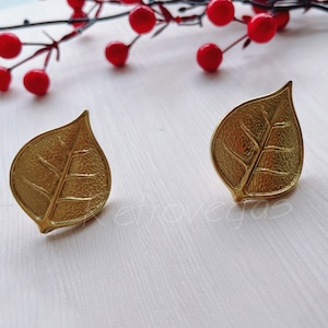 Könnte beinhalten: Ein Paar goldene Ohrringe in Blattform. Die Ohrringe sind aus Metall und haben eine strukturierte Oberfläche.