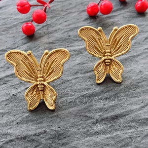May include: A pair of gold butterfly earrings. The earrings are detailed with a textured design and have a delicate, feminine look.