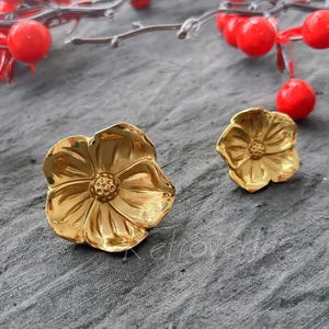 May include: A pair of gold-tone flower-shaped earrings. The earrings are made of metal and have a delicate, feminine design.